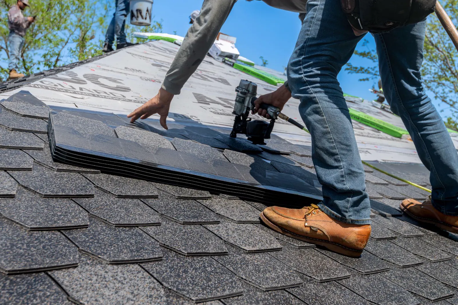 Roofer nailing new architectural shingles over fresh underlayment
