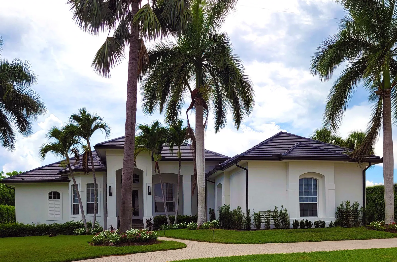 White Florida home with a dark flat tile roof and palm trees